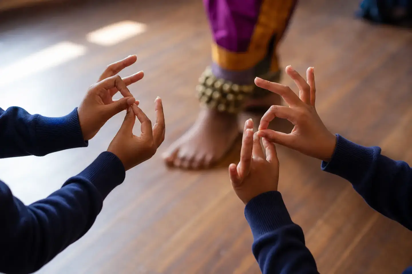Close view of pupils' hands held in an Indian dance gesture, with a facilitator demonstrating out of focus behind them.